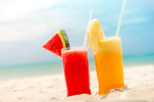 Zwei Fruchtsäfte stehen auf dem Sand. Im Hintergrund ist das Meer